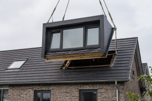 Prefab kunststof dakkapel wordt met een kraan op een schuin dak geplaatst